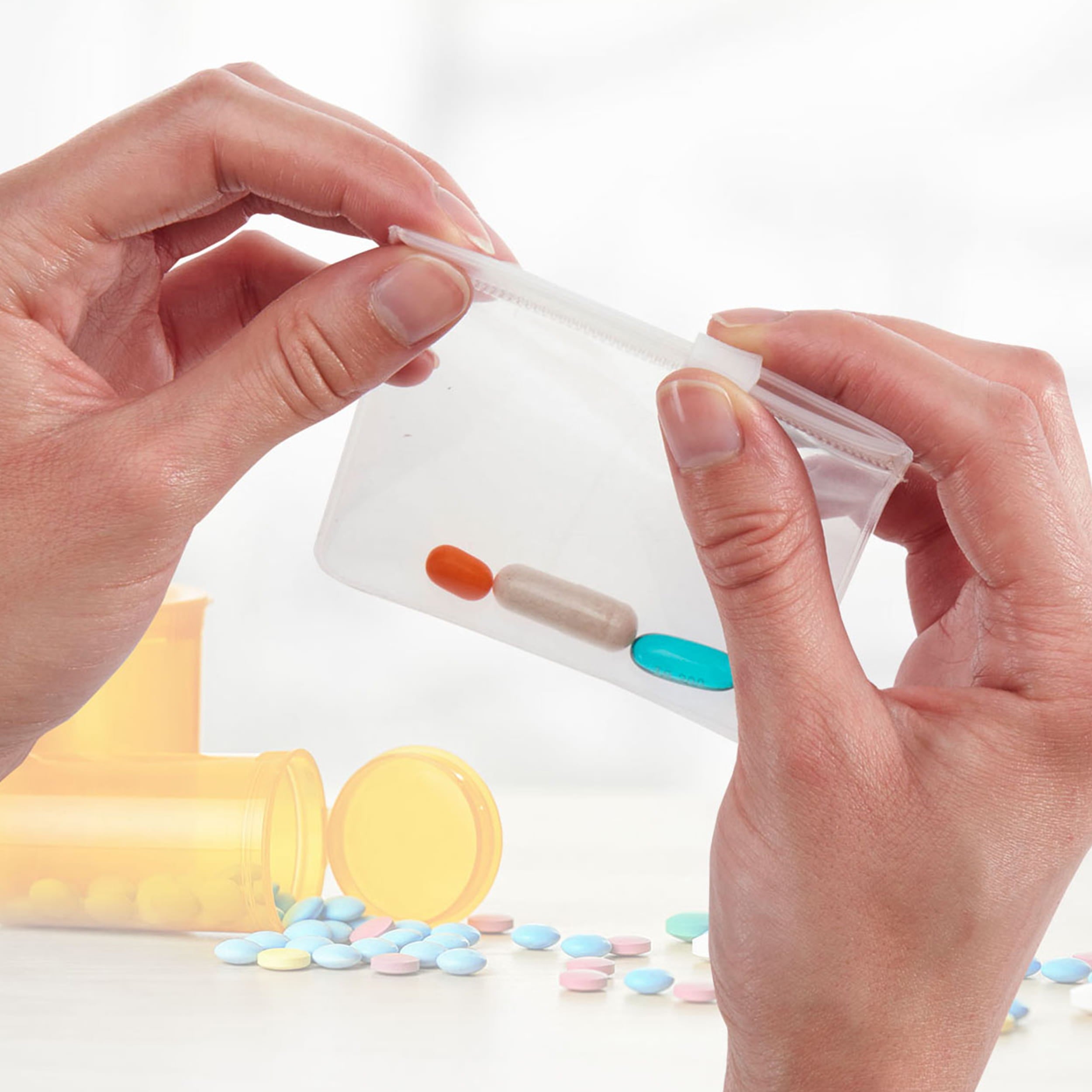Hands holding a small transparent container with colorful pills featuring the Zippered Pill Pouch for sale by Talus.