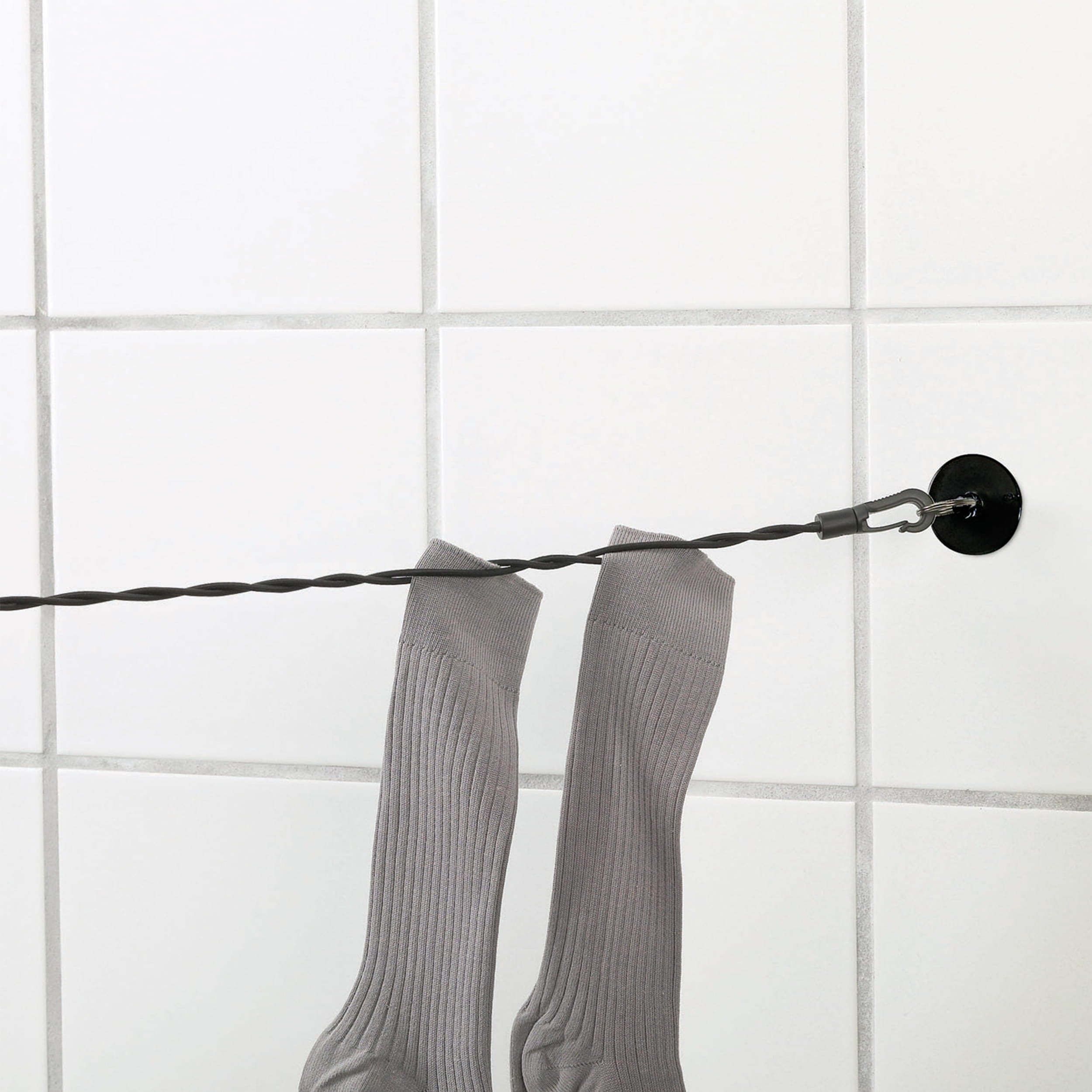 Gray socks hanging on a black wire against a white tiled wall.